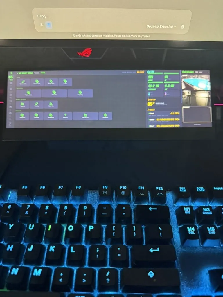 The Batcave Deck running below the primary OLED monitor — showing the app launcher, system stats, weather, mining telemetry, and live print farm camera feed